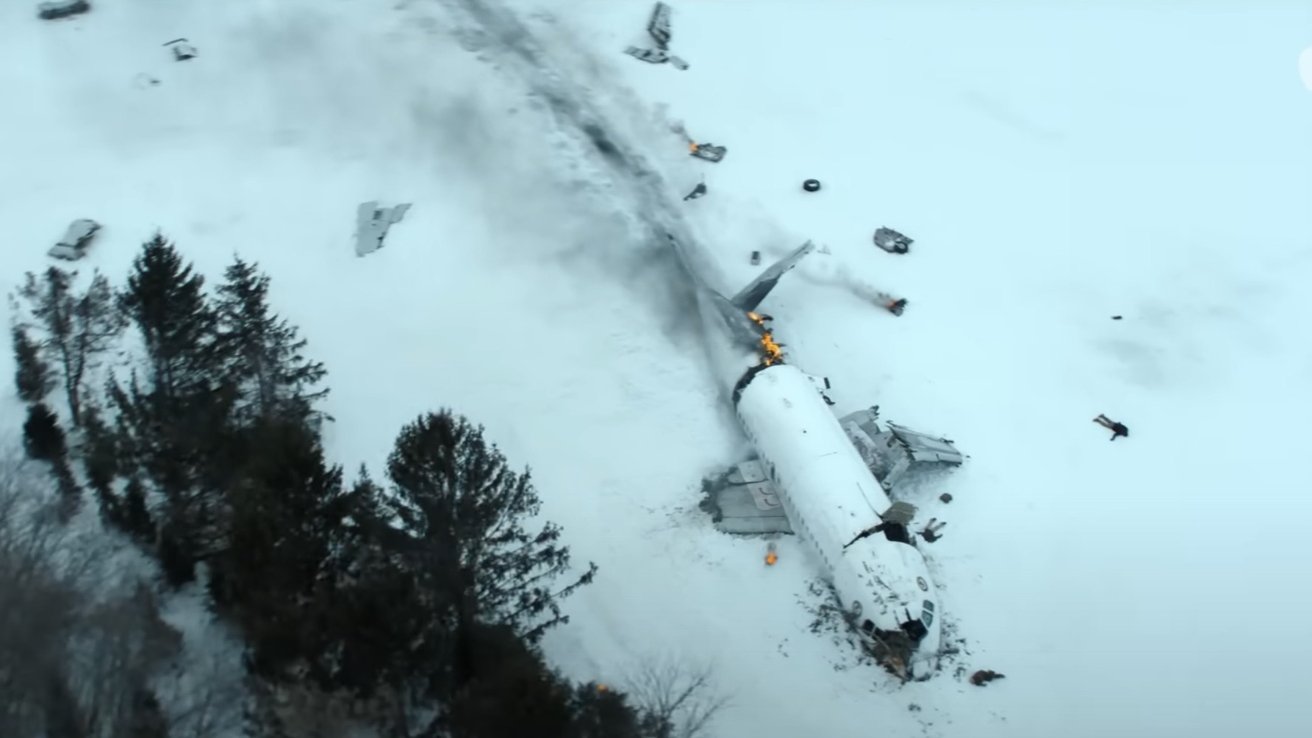 Aerial view of a plane crash site on snow with debris scattered, smoke rising, and some areas on fire near trees.