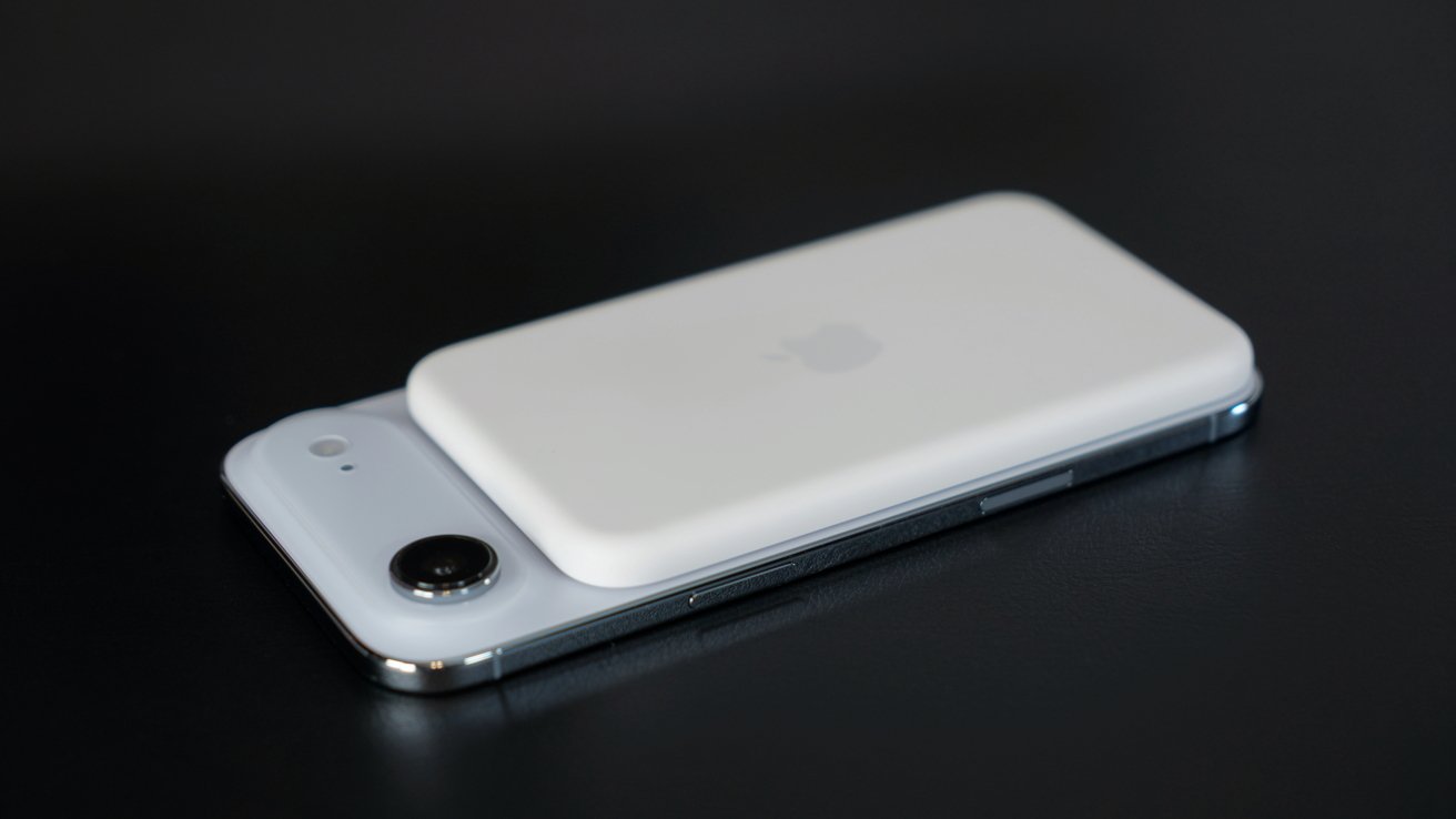 A smartphone lies on its back with a white rectangular accessory on top, featuring rounded edges and an embossed logo, against a dark surface.