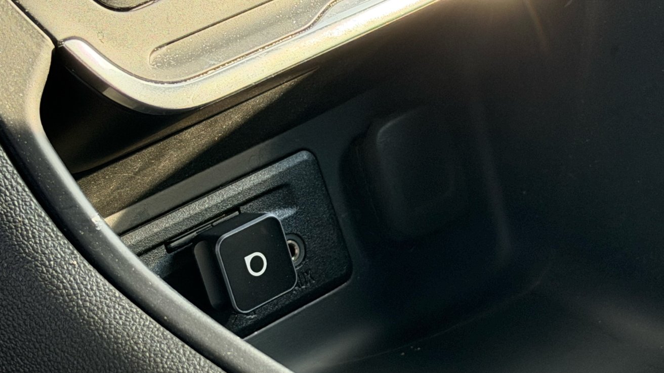 Car interior with a close-up view of a USB charging port featuring a circle icon on a black square button.