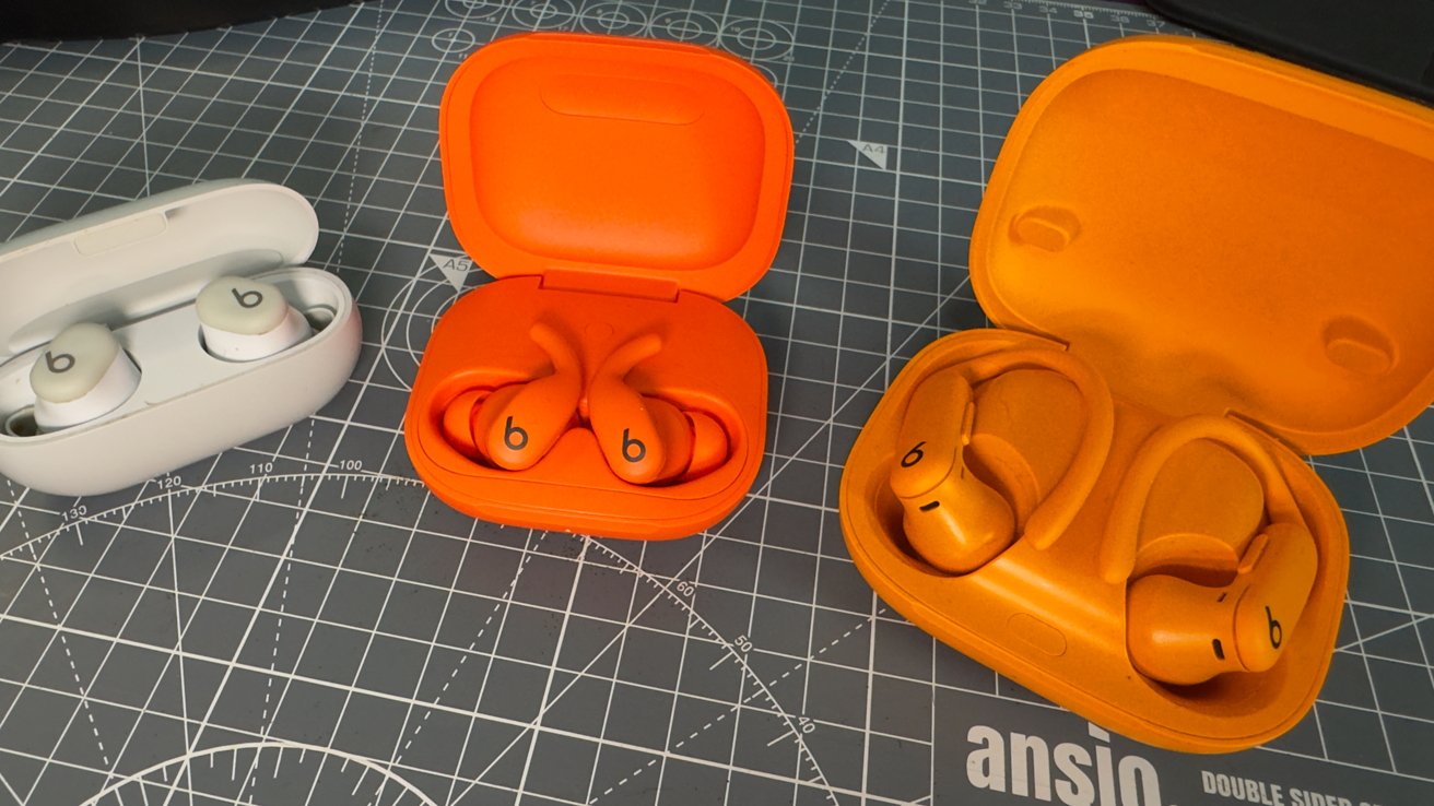 Three pairs of wireless earbuds with charging cases on a grid-patterned mat: one white pair, two orange pairs.