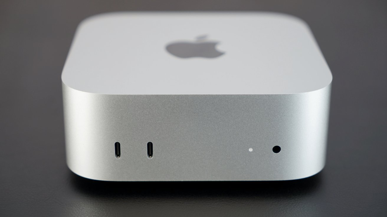Silver compact computer with rounded edges, Apple logo on top, two small ports, and indicator light on the front.