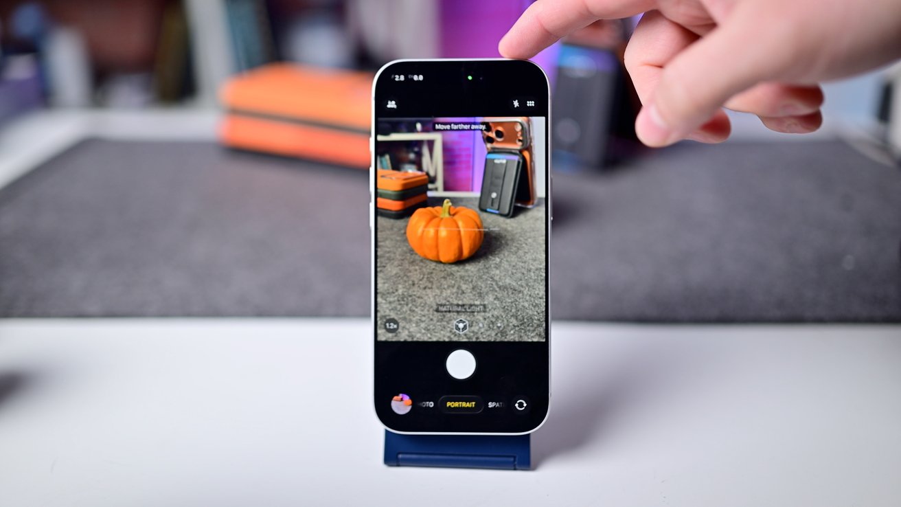 Smartphone displaying a small pumpkin with a blurred background, held by a hand pointing at the screen.