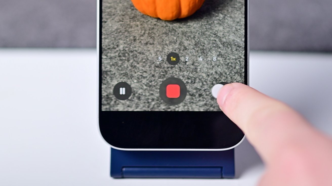 A finger touches a phone screen showing a small pumpkin, with video recording controls visible.