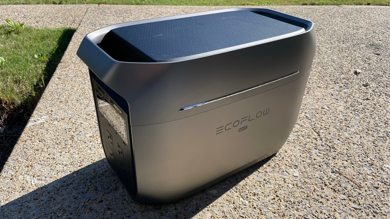 Portable power station with a sleek design, labeled 'EcoFlow Max,' resting on textured concrete, surrounded by grass.