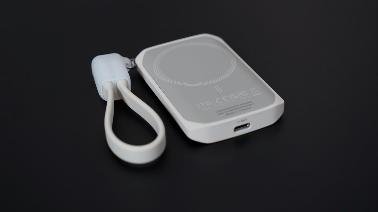 A white portable hard drive with a circular design and attached looped strap, resting on a black surface.