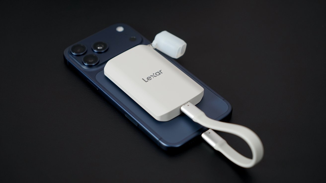 A black smartphone sits on a dark surface with a white Lexar external storage device connected by a curved cable on top.