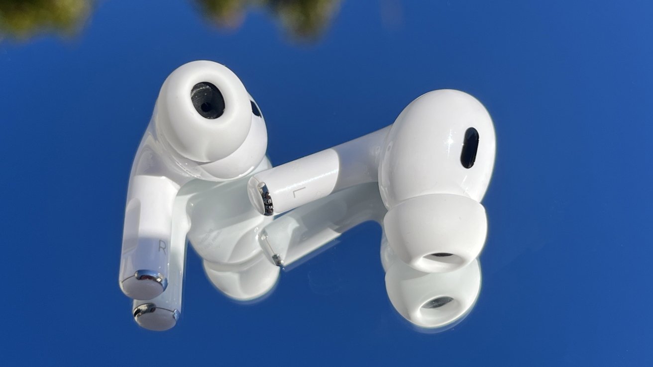 Two white wireless earbuds rest on a reflective surface against a bright blue background.