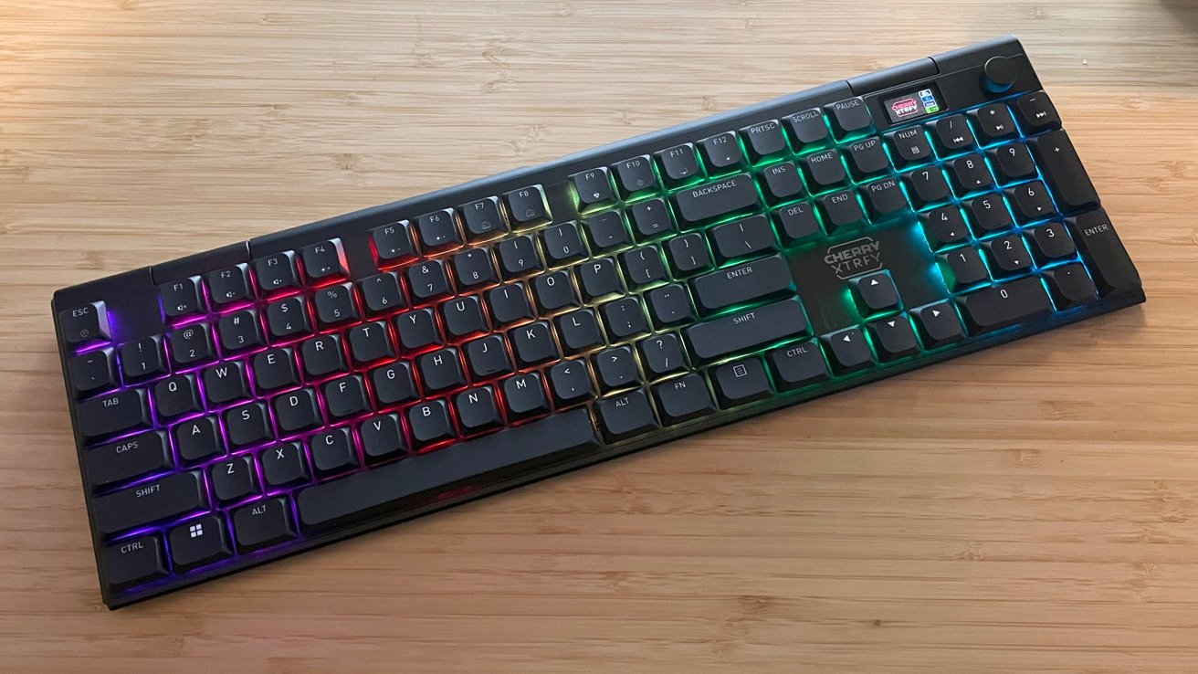 RGB backlit mechanical keyboard on wooden surface, keys glowing in various colors including purple, red, green, and blue.