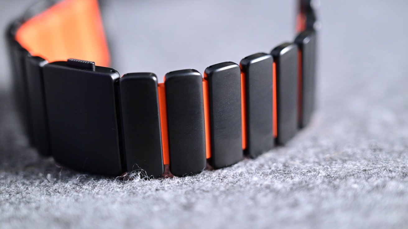 Black watch strap with orange accents on a textured gray surface with rectangular links and a modern design.