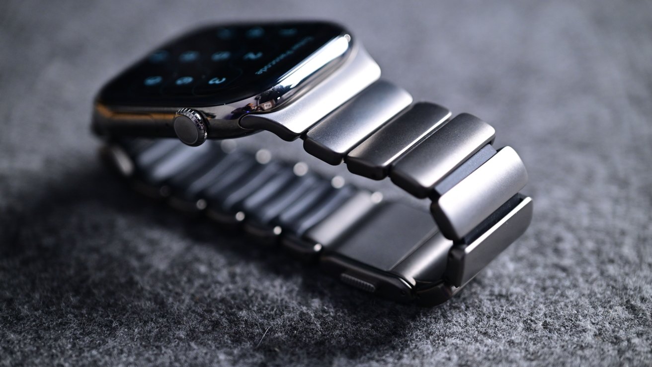 A smart watch with an elegant metal band and a digital display that rests on a soft gray fabric surface.