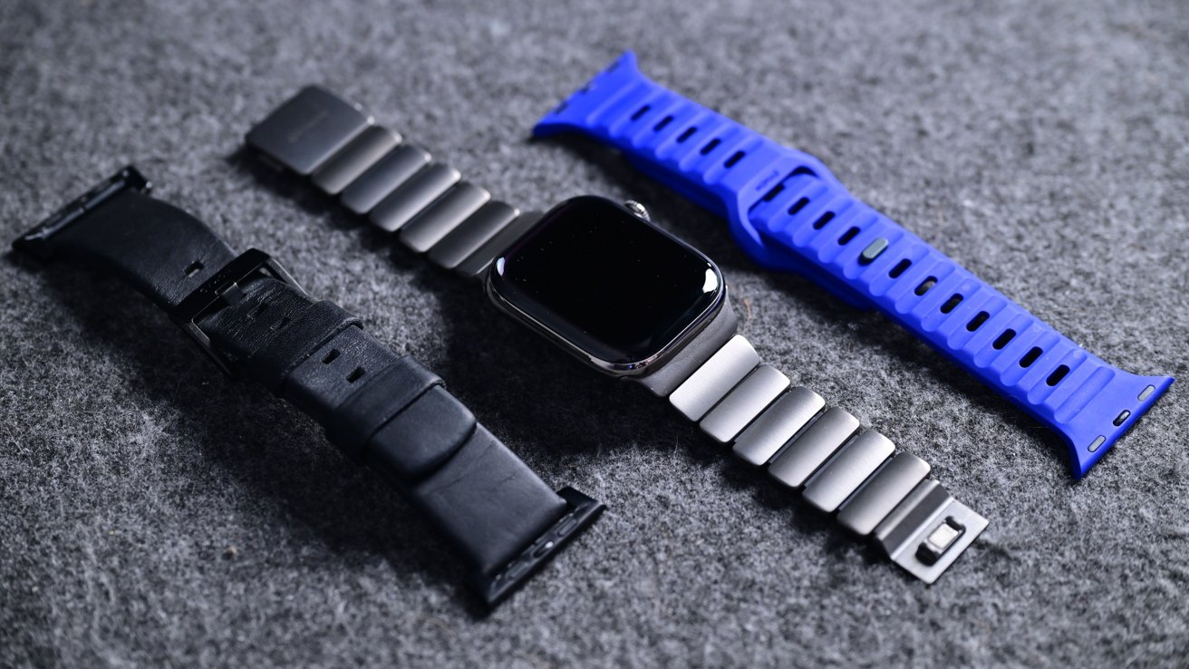 Smart watch with a metal band, lined with leather and blue silicone straps on a gray surface.