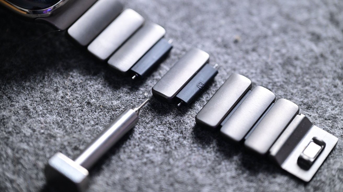 Bracelet links and a small screwdriver on a gray felt surface.