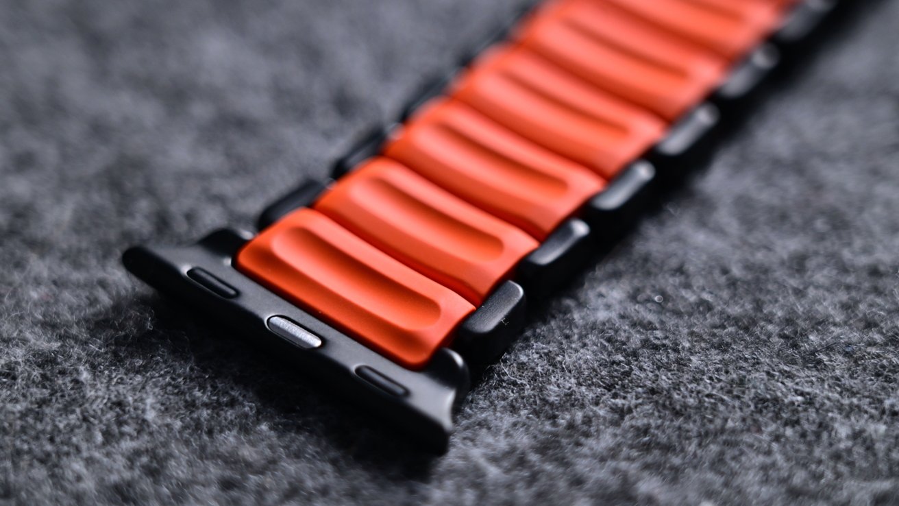 Close-up of an orange and black watch strap with a textured wavy design on a gray blurred surface.