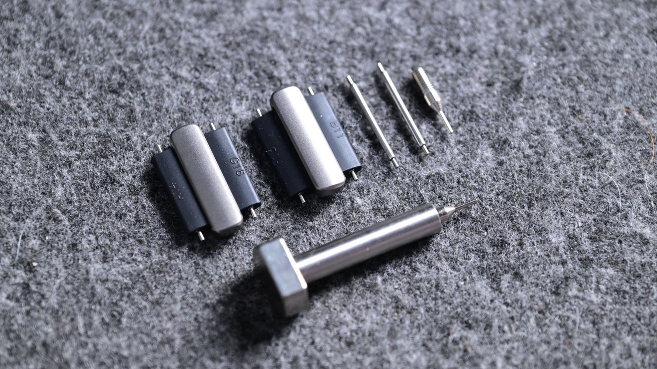 Metal tools including hex screw, cylindrical handles and small drill bits on gray textured surface.