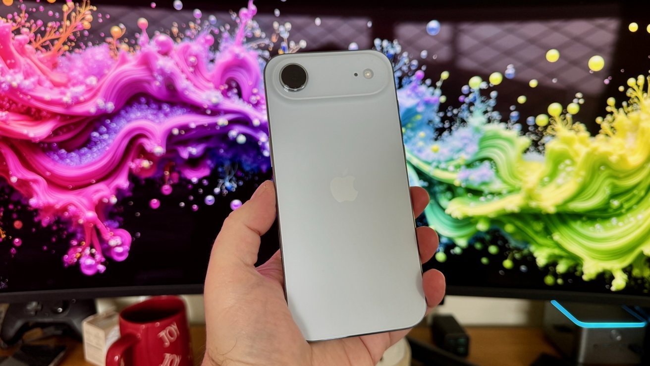 A hand holds a silver smartphone with an Apple logo, against a vibrant, multicolored abstract background.