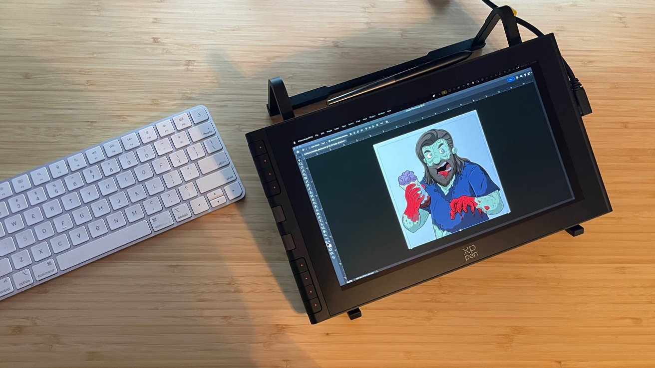 Digital drawing tablet displaying cartoon zombie holding a brain is placed on a wooden desk next to a white keyboard.