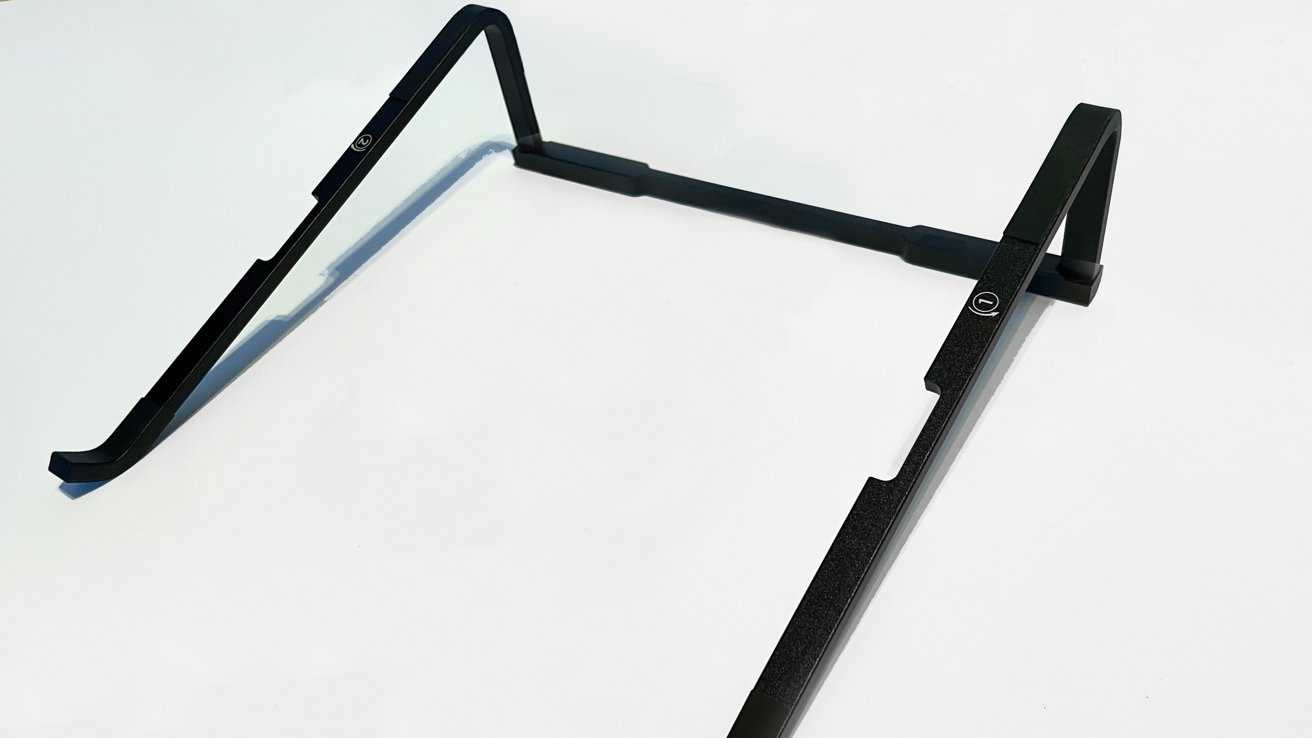 A black, angular frame resembling an inverted 'V' stands on a white surface, casting a shadow.