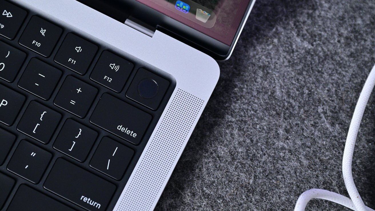 Laptop keyboard and part of a touchpad with volume control keys, delete key, speaker grill, and gray fabric surface in the background.