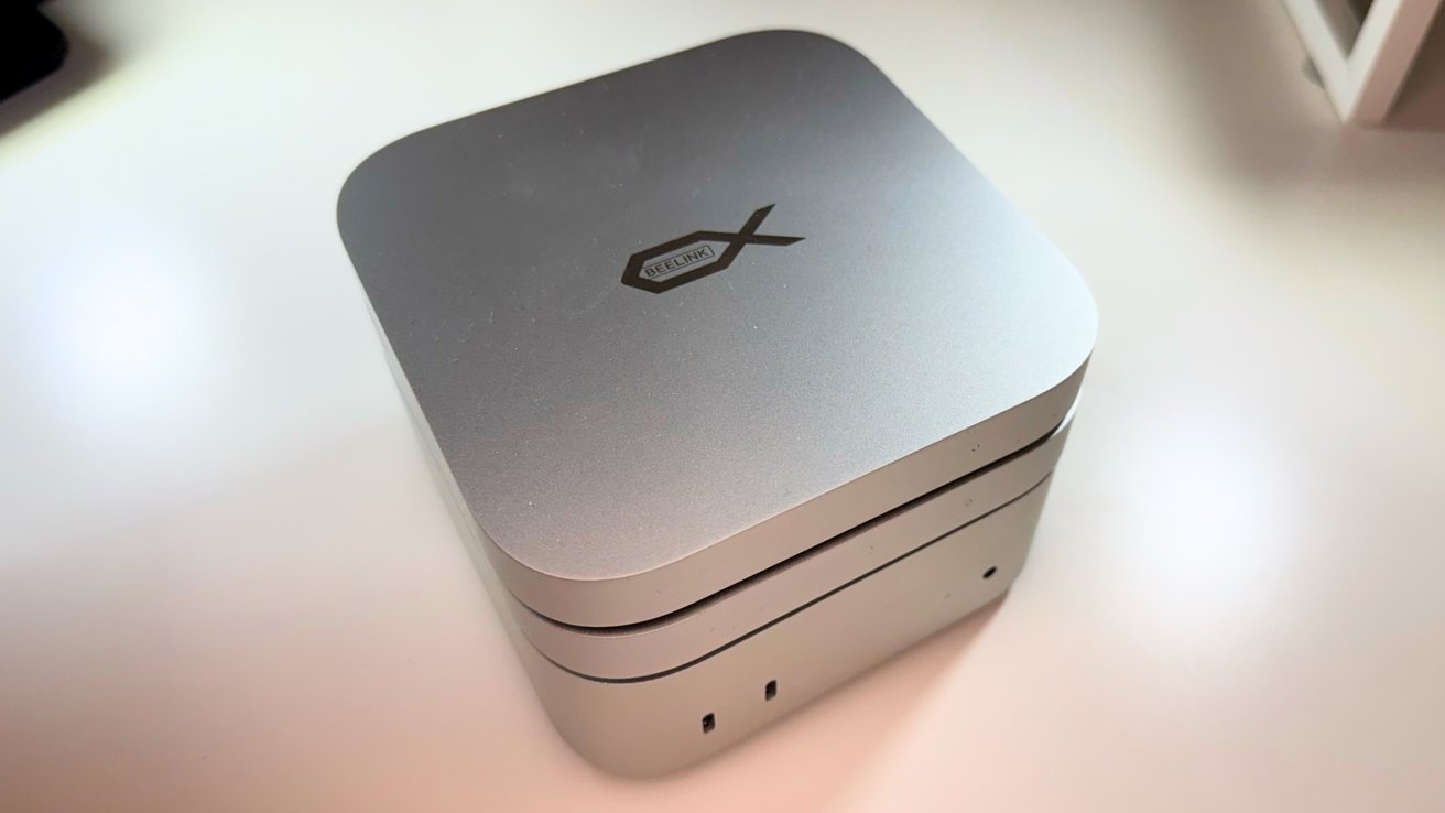 Small, silver, rounded square electronic device with two stacked layers, featuring a logo on top, placed on a white surface.