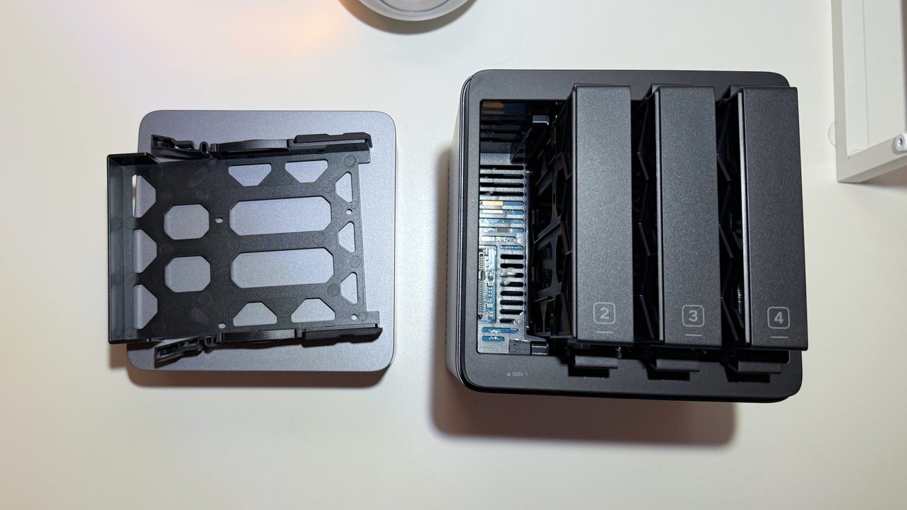 Open four-bay network attached storage device with one drive caddy removed, exposing internal circuitry, on a white surface.