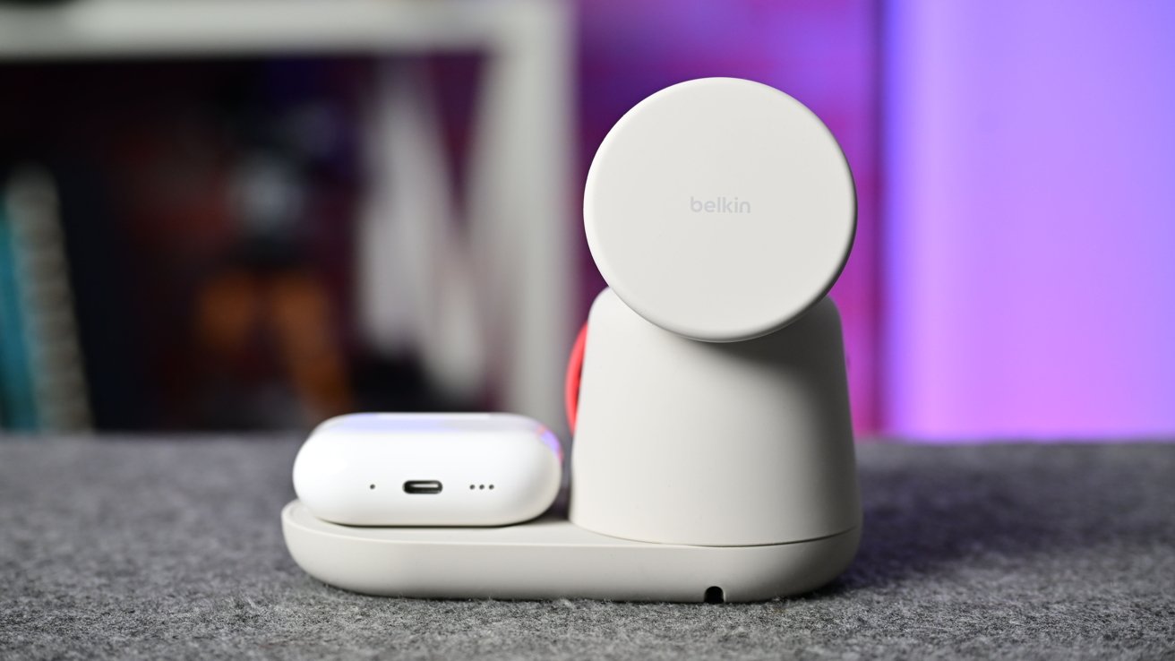 White wireless charging station with round stand and small charger on a gray surface, set against a blurred pink and purple background.