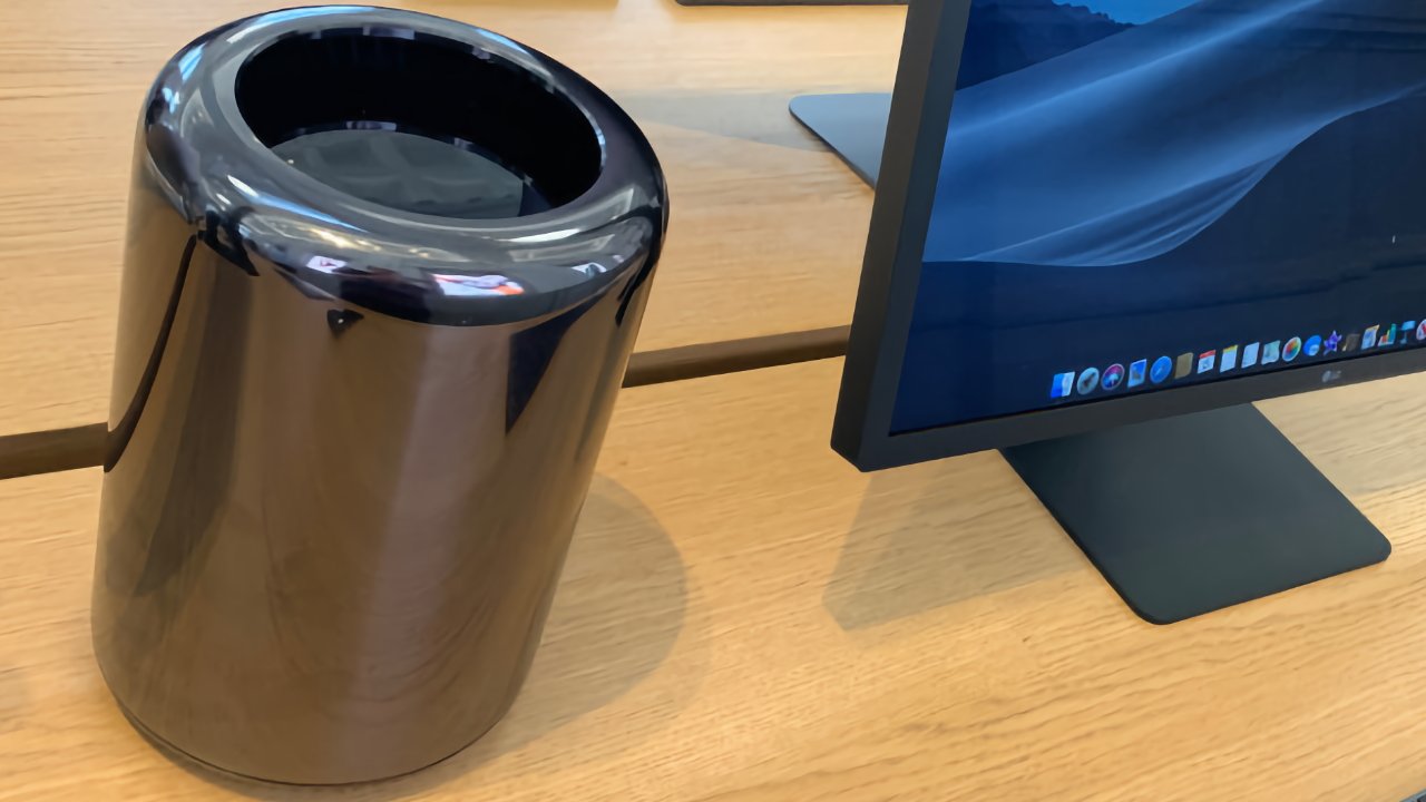 Elegante computadora cilíndrica junto a un monitor sobre un escritorio de madera, que muestra una pantalla de escritorio.