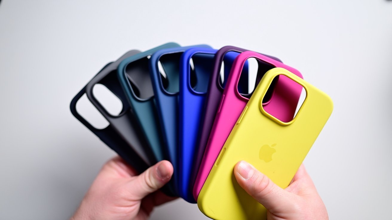 Hands holding six colorful phone cases, fanned out in dark green, navy, blue, purple, magenta, and yellow against a plain background.