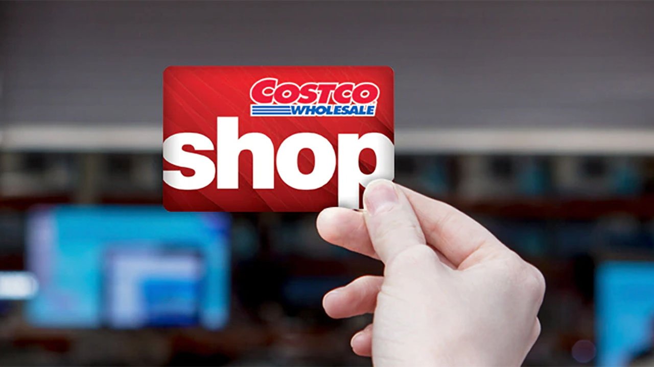 Hand holding Costco Wholesale gift card with the word Shop in bold letters on a blurred background.