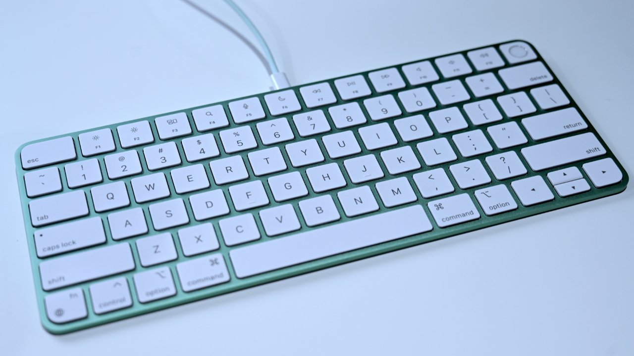 A compact white keyboard with a green frame, featuring white keys and a minimalist design, connected through a white cable on a light background.