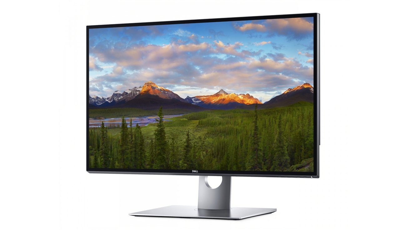 A monitor showing a picturesque mountain landscape with a brilliant sunset, blue sky and green forest. The screen is elegant with a modern minimalist stand.