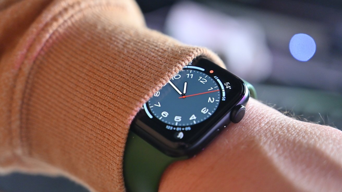 A wrist with a black smartwatch partially covered by a brown sleeve, displaying an analog clock face and temperature.