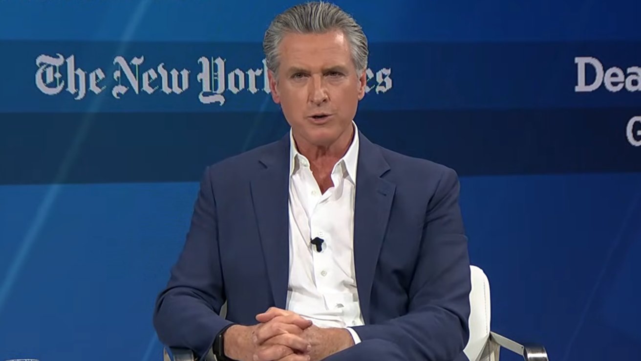 Man in a suit speaking, seated on a chair against a blue background with 'The New York Times' logo visible.