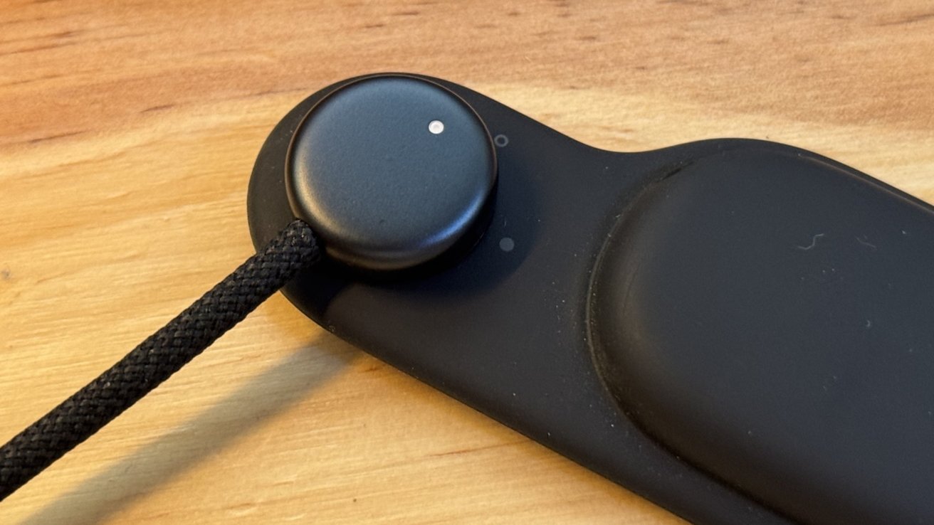 Black circular button on a dark rectangular base with a black cord, resting on a wooden surface.