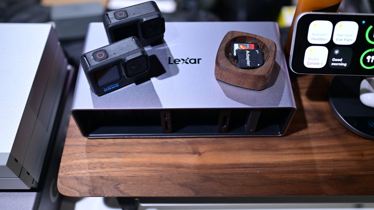 Two action cameras and a memory card in a wooden holder on a table with a Lexar device, beside a screen showing various app icons.