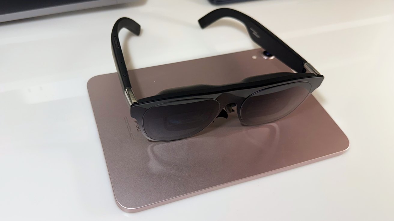 Black sunglasses resting on a closed, light pink laptop, placed on a white surface.