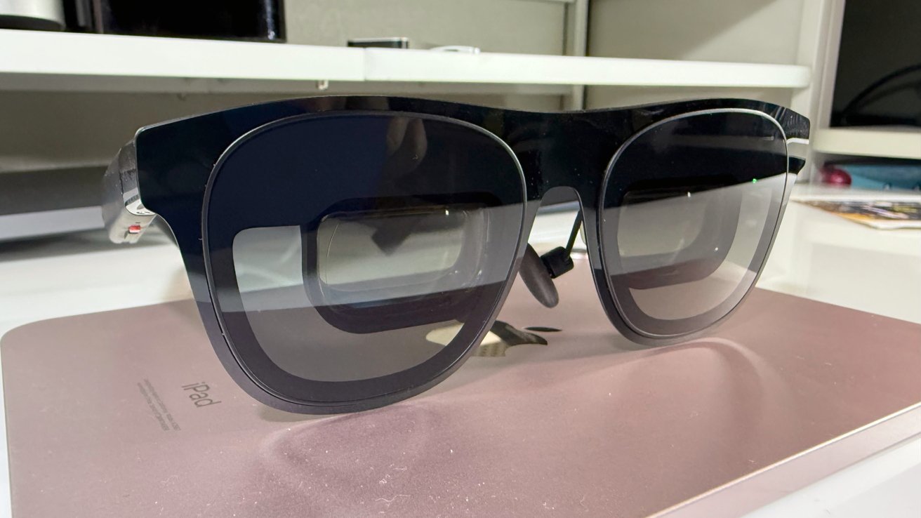 Black sunglasses with thick frames on a pink iPad, placed on a white table.