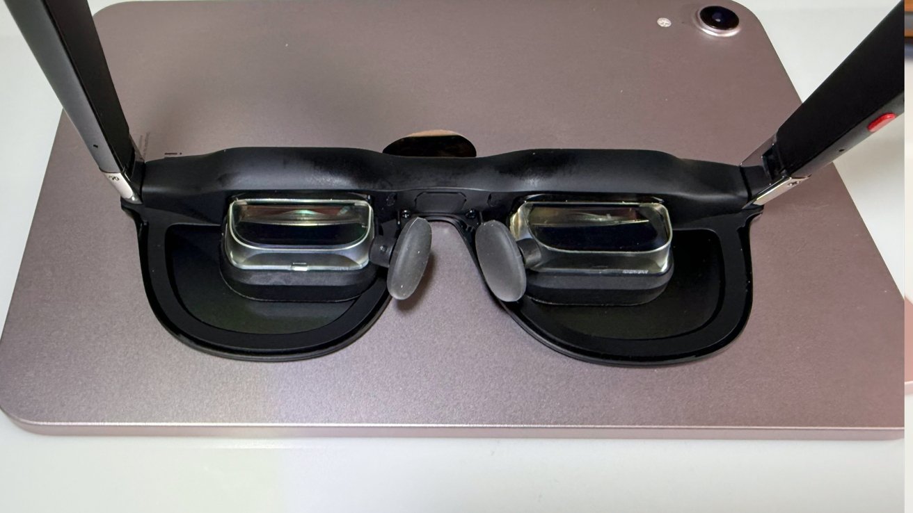 AR glasses with transparent lenses and a black frame placed on a metal surface when viewed from above.