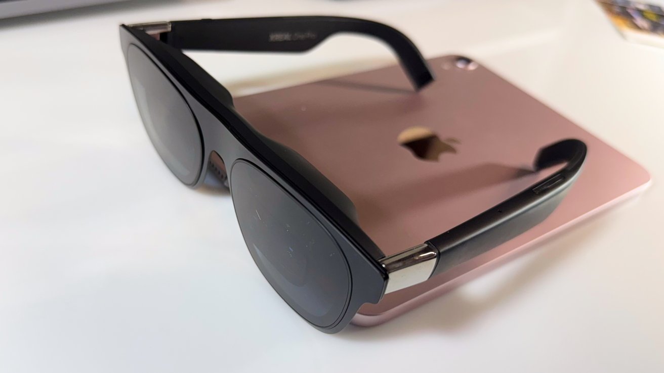 Black sunglasses on a rose gold tablet with a partially visible apple logo on a white surface.