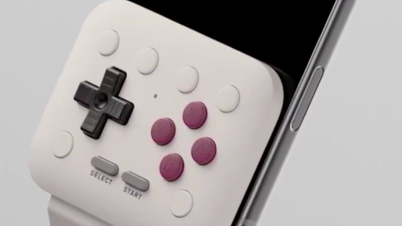 Close-up of an attached gaming controller with a directional pad, four pink circular buttons, and select-start buttons on a white background.