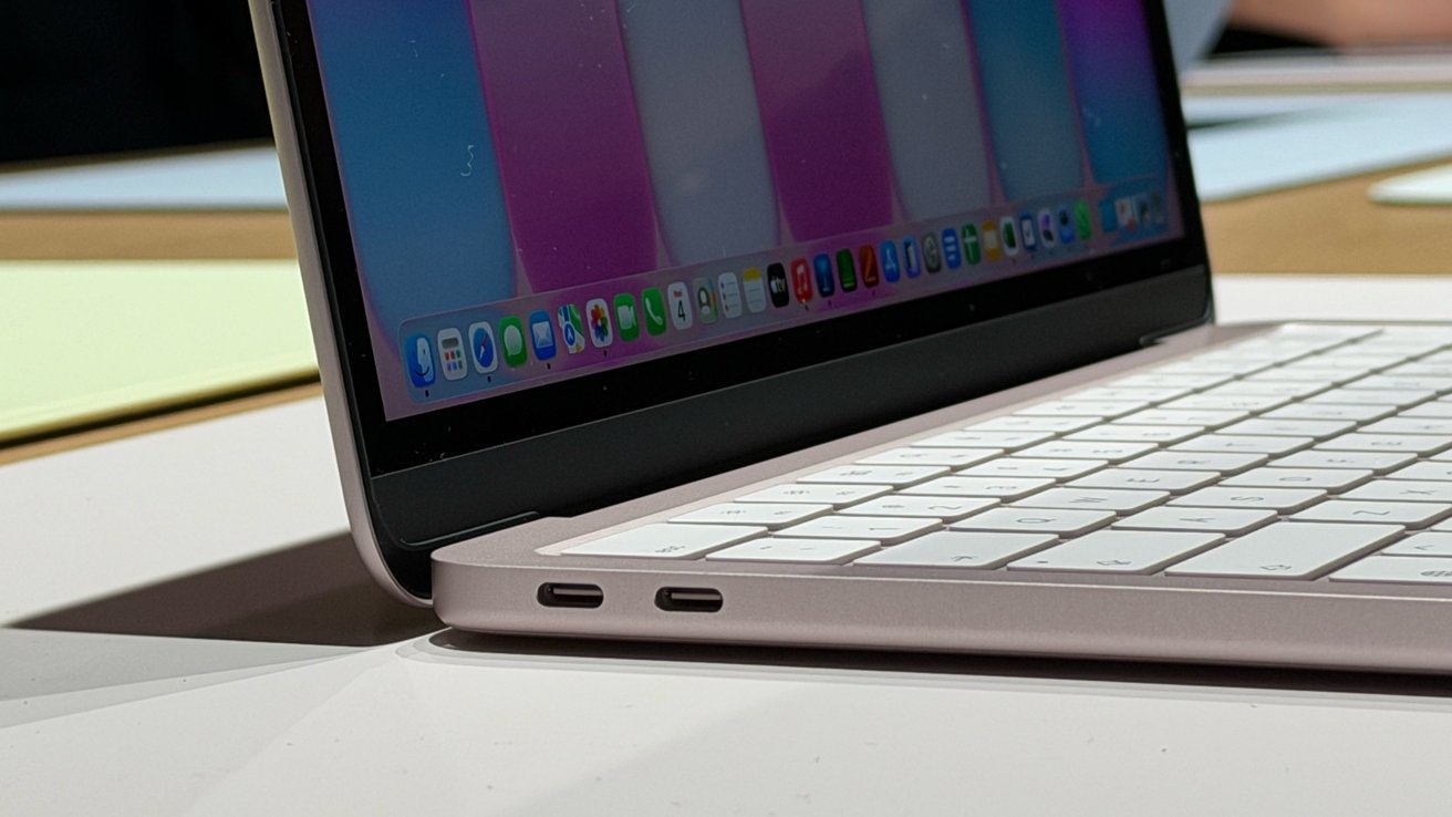 Side view of an open slim laptop with white keyboard, two USB-C ports on the left edge, and a colorful desktop screen, resting on a smooth reflective table