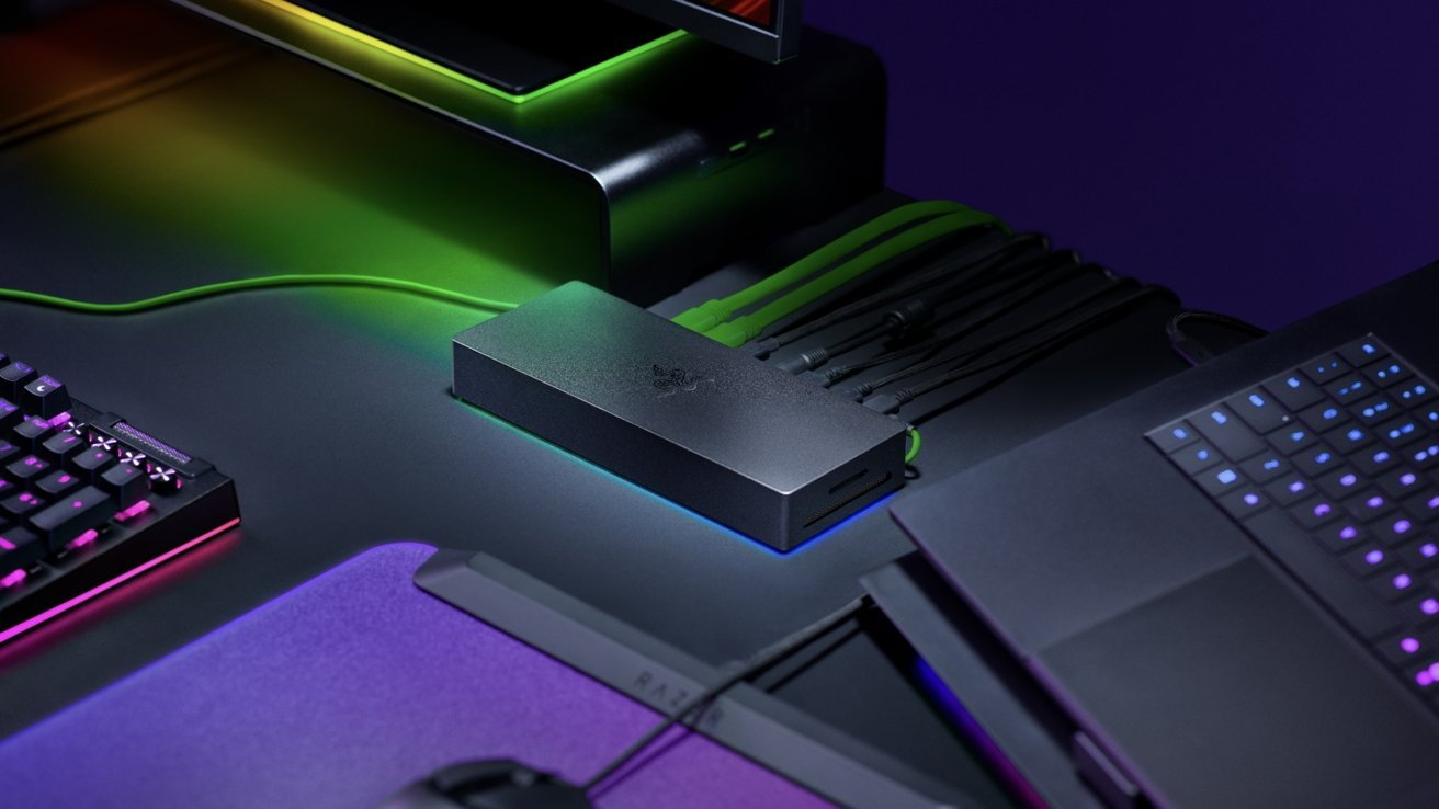 Sleek Razer docking station on a gaming desk, connected to a laptop, keyboard, and monitor, with green and purple RGB lighting illuminating cables and accessories