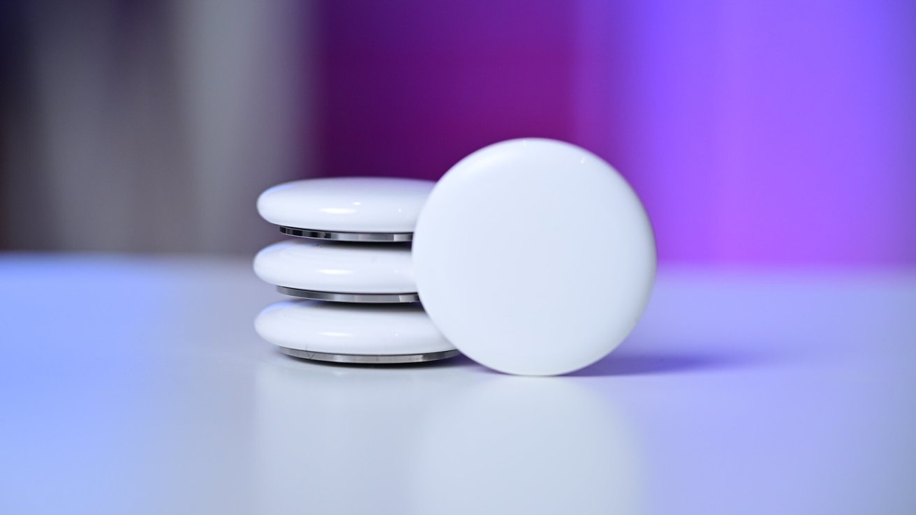 Four round white tracking tags stacked on a smooth surface, one leaning in front, with a soft blurred background glowing in gradients of purple and blue.