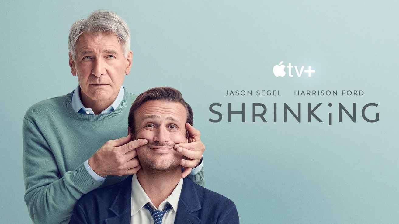 Older man in sweater stands behind younger man in suit, gently stretching his cheeks into a forced smile, with Apple TV Plus series title Shrinking and actors names on pale blue background