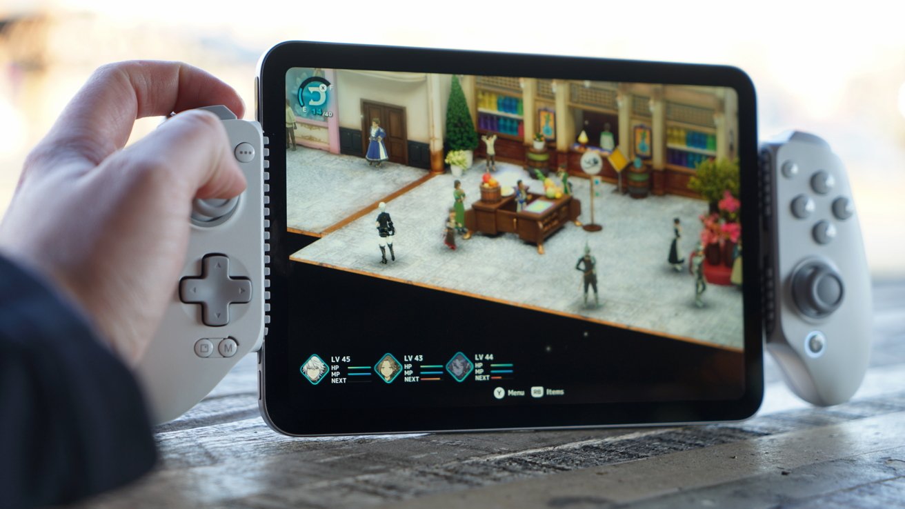 Hand holding tablet with white game controllers attached, playing colorful fantasy role-playing game showing characters in close-up indoor market scene on screen