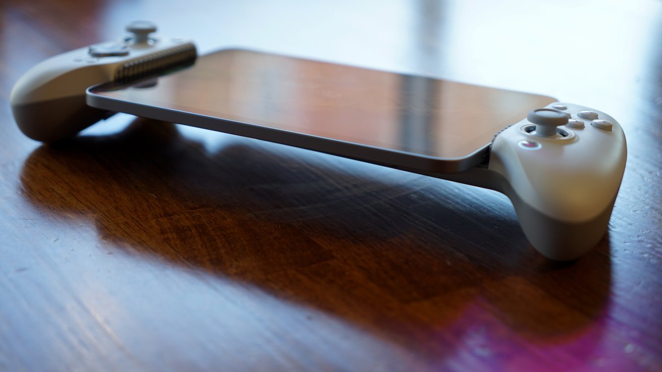 Hand-held gaming device with white controllers attached to either side of a large reflective screen, resting on a polished wooden table in soft natural light