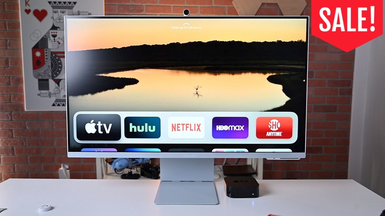 Samsung M8 Monitor on a desk showing Apple TV home screen with apps like Hulu, Netflix, HBO Max, and Showtime; SALE banner in upper right against brick wall background