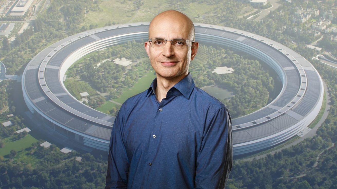 Bald man with glasses wearing a blue button-up shirt, smiling confidently, standing against an aerial view of a large circular futuristic office complex surrounded by greenery