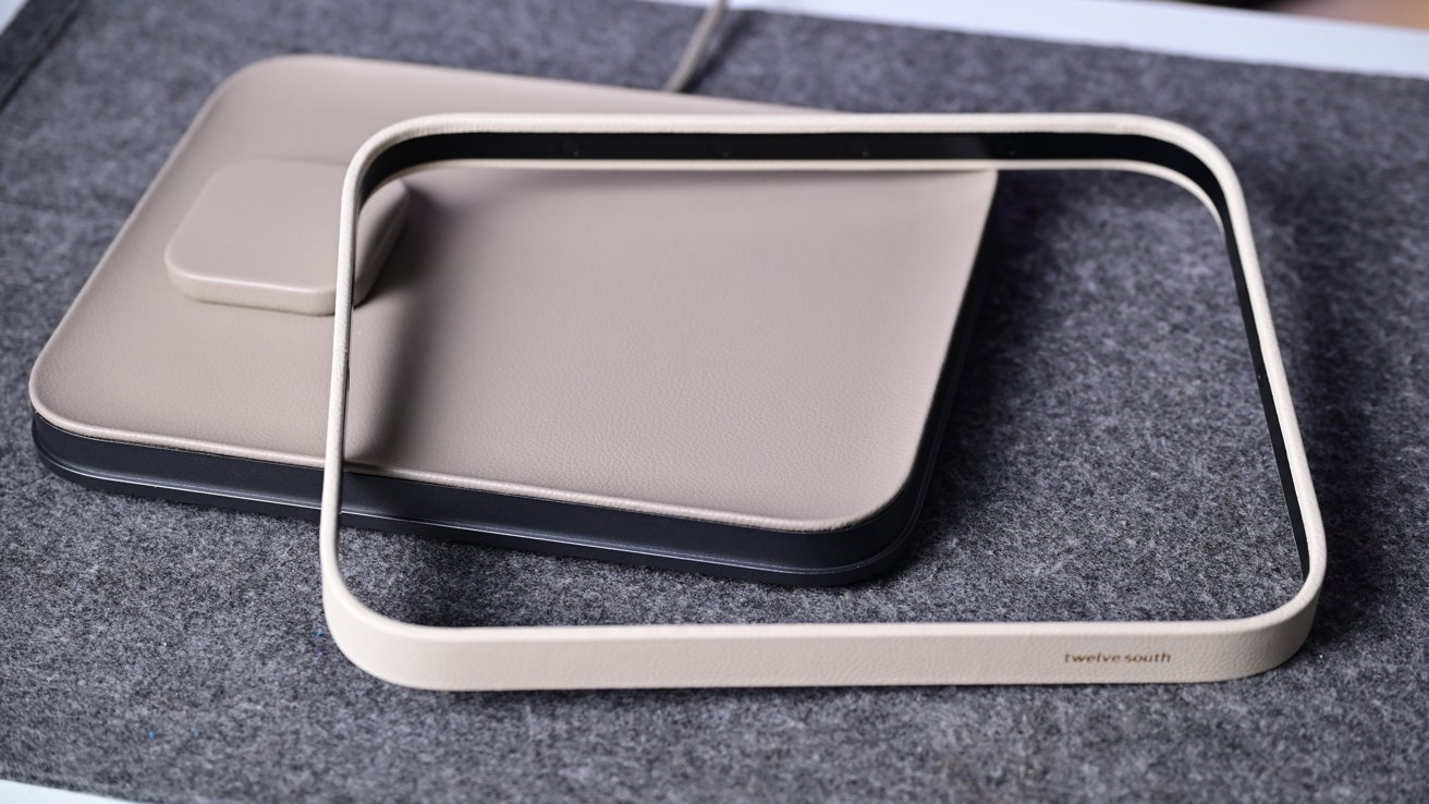 A rectangular beige wireless charging pad on a gray fabric surface with a matching rectangular frame that stays diagonally on top shows a minimalist modern design and smooth rounded edges