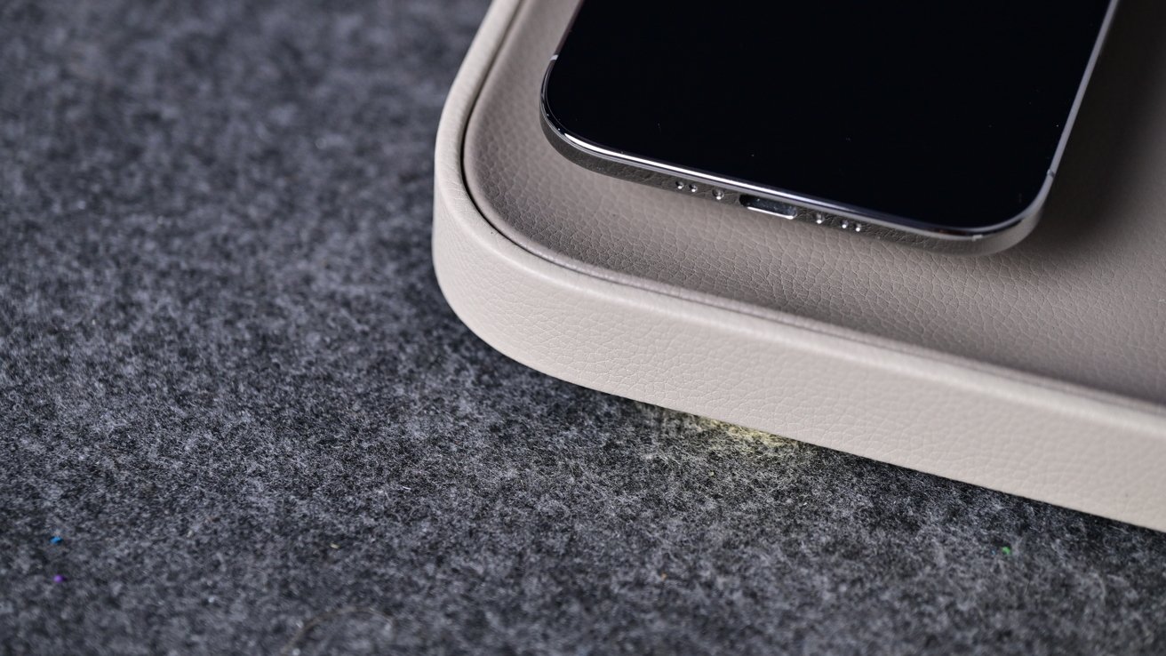 A smartphone placed on the corner of a light gray wireless charging pad, placed on a soft dark gray felt surface, close up view from above
