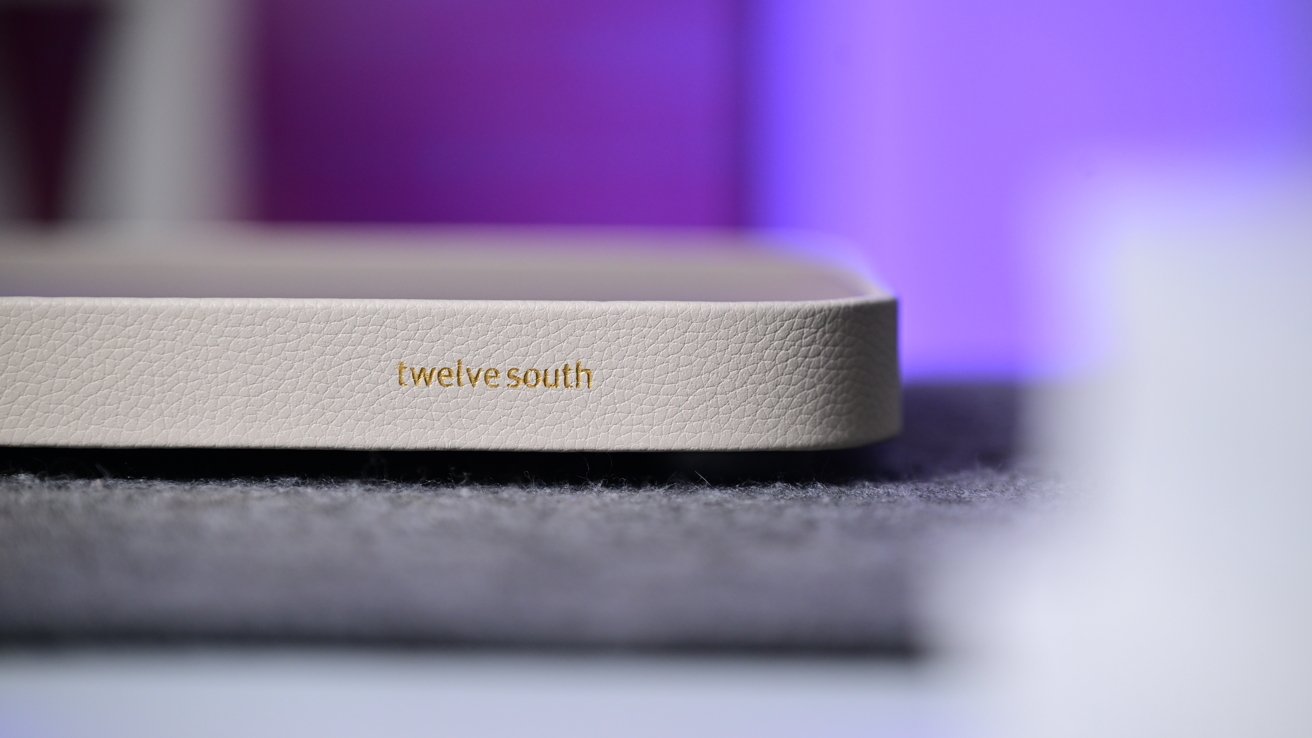 Close-up of a beige Twelve South device with a textured finish lying on a gray cloth pad against a softly blurred purple and blue background